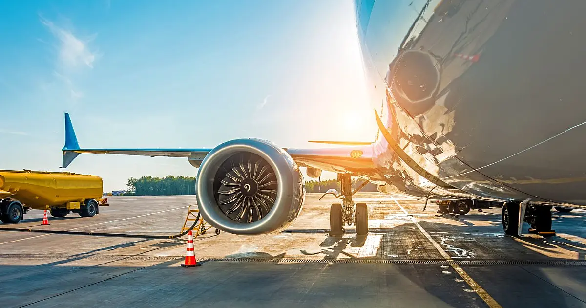 Avião sendo abastecido em aeroporto durante pôr do sol antes de voo internacional.