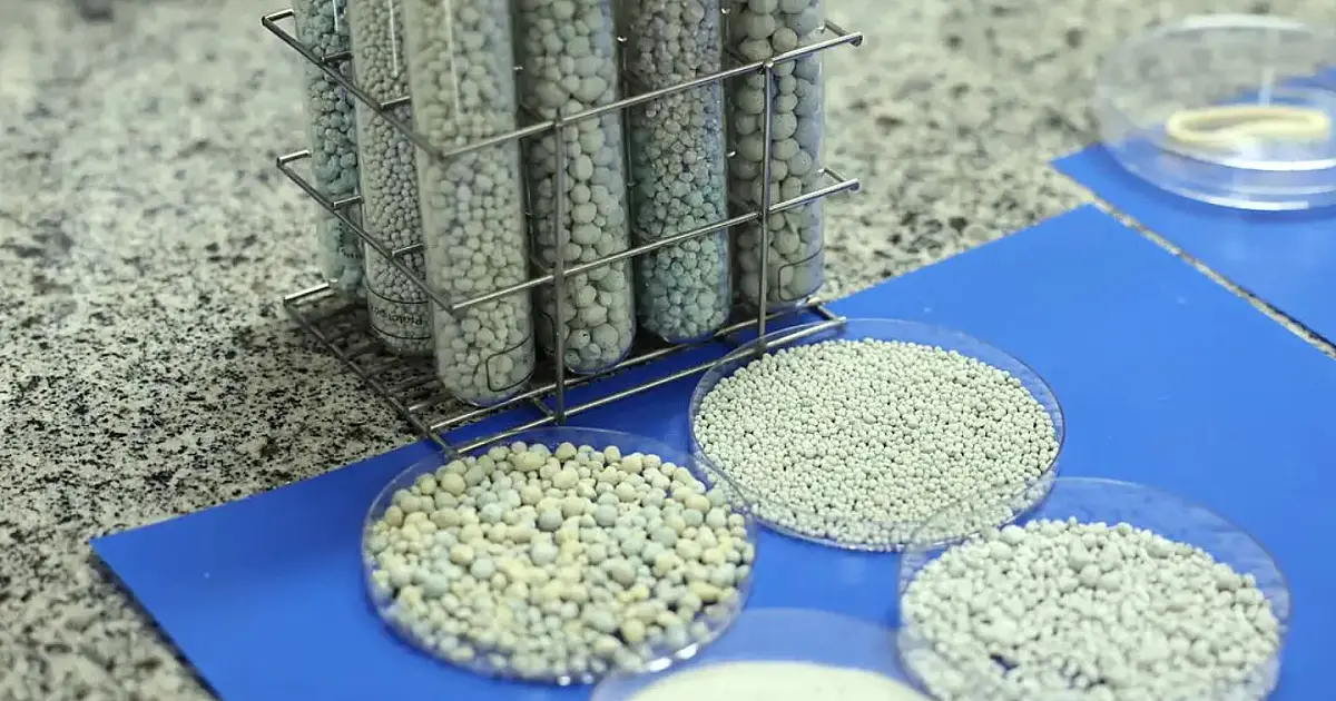 close-up focado nas mãos de um pesquisador vestindo luvas de látex brancas, manipulando pequenas amostras de grânulos minerais dentro de um laboratório científico moderno.