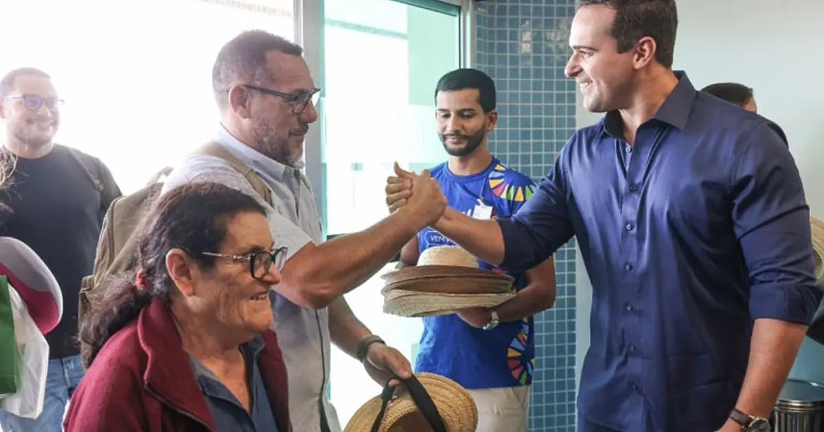 Aeronave comercial de grande porte estacionada na pista do aeroporto sob a luz do dia, com equipes de apoio e autoridades posicionadas próximas à escada de desembarque.