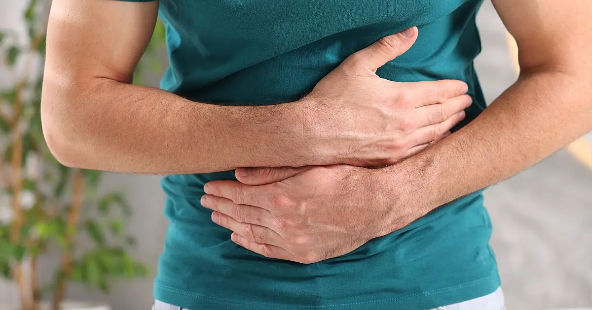 Homem com dores e desconforto abdominal segurando a barriga em banheiro.