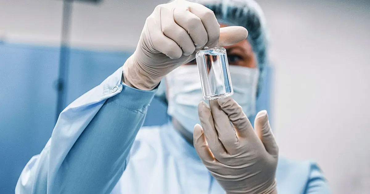 Profissional de saúde segurando frasco relacionado ao tratamento do vírus ebola durante alerta da OMS.