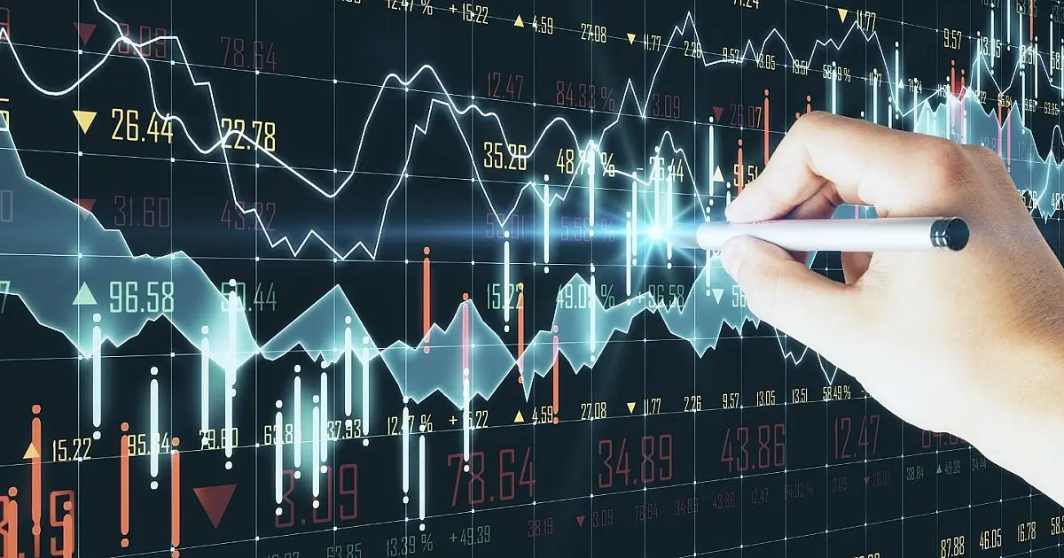 Monitor exibindo gráficos de barras e linhas ascendentes e descendentes em tons de azul e vermelho com dados econômicos.