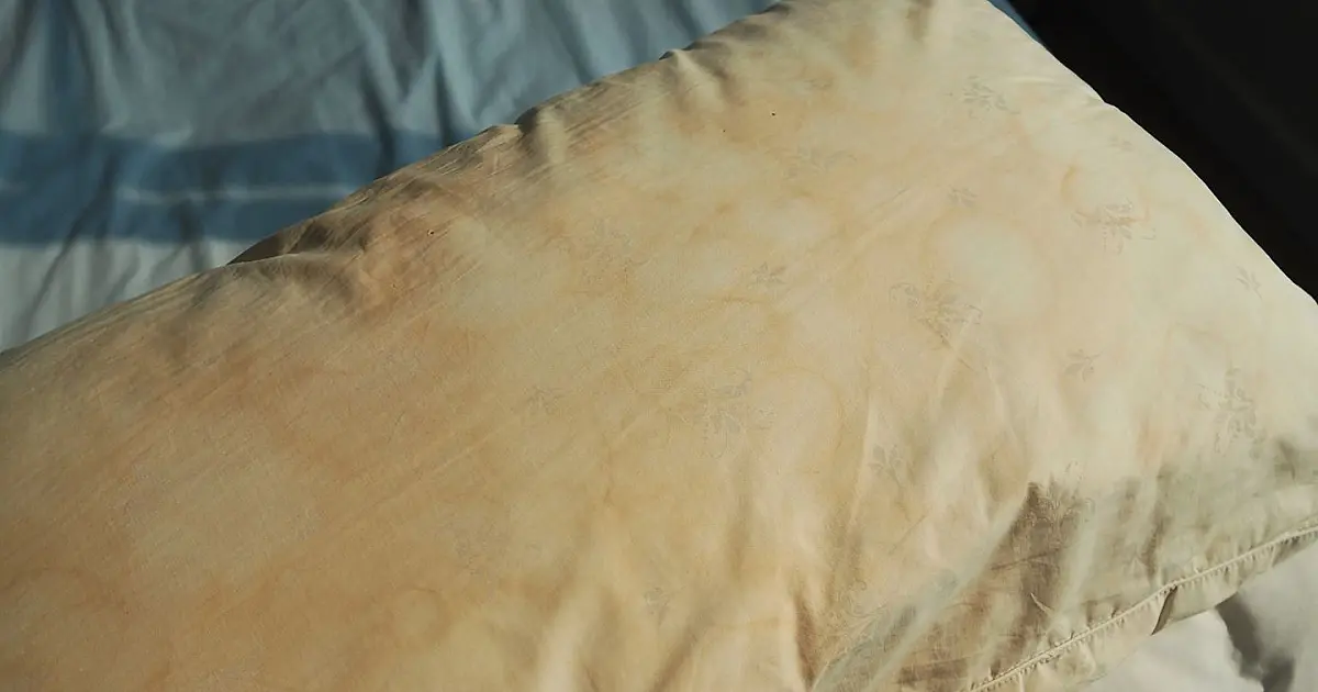 Travesseiro com manchas amareladas sobre cama representando limpeza doméstica caseira.