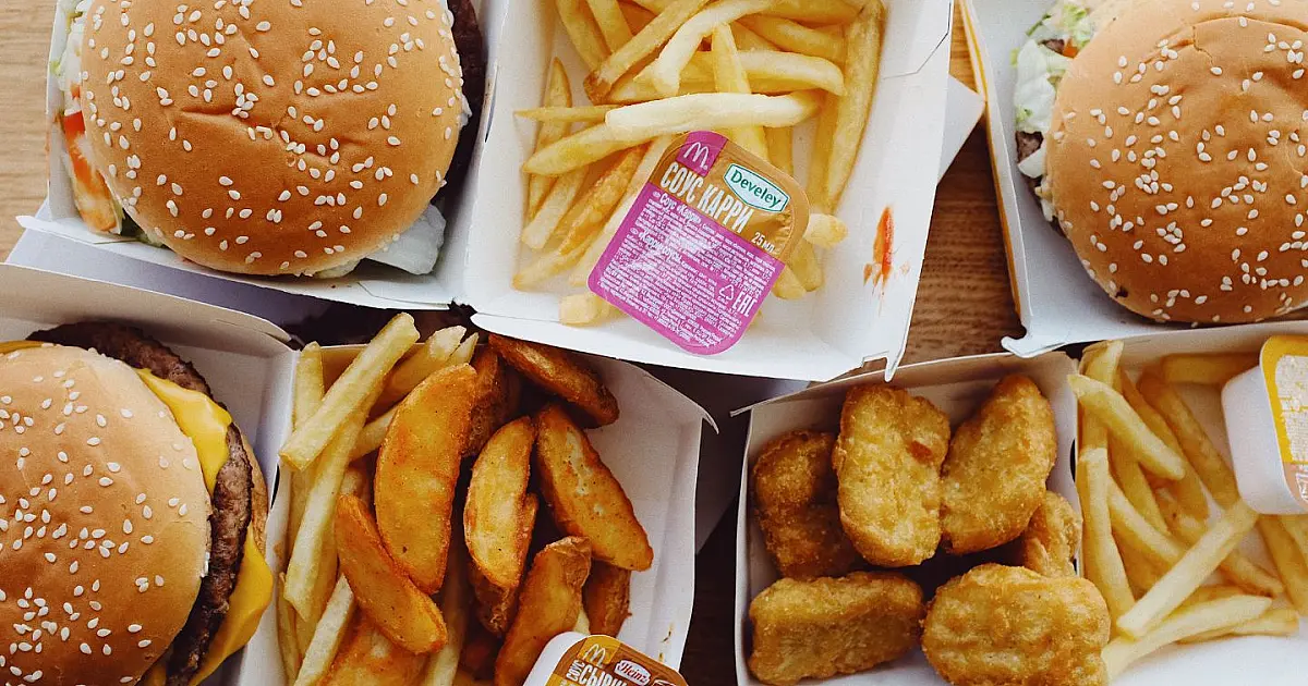 Uma mesa de madeira escura com um combo de fast-food contendo hambúrguer, batatas fritas e um copo de refrigerante com gelo.