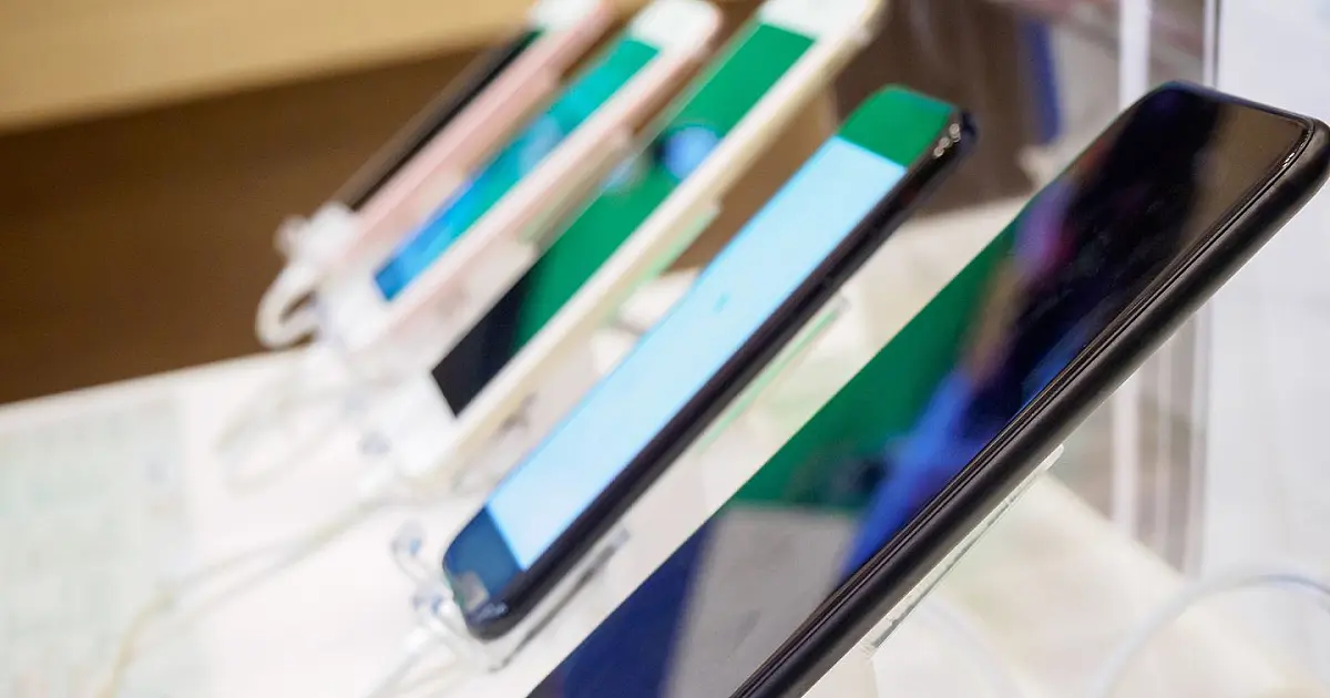 Vários smartphones modernos de diferentes marcas e tamanhos dispostos lado a lado em uma bancada de exibição iluminada dentro de uma loja de eletrônicos
