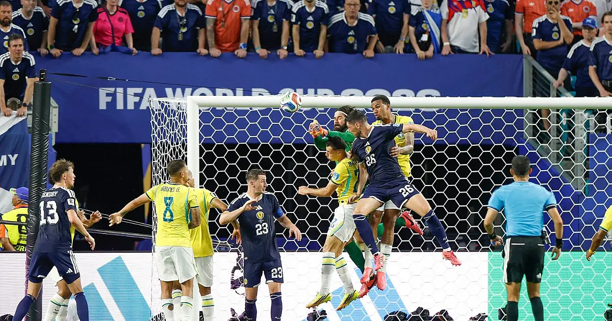 O goleiro brasileiro Alisson, vestindo uniforme verde, salta na grande área para dar um soco na bola e afastar o perigo durante partida de futebol sob iluminação de refletores