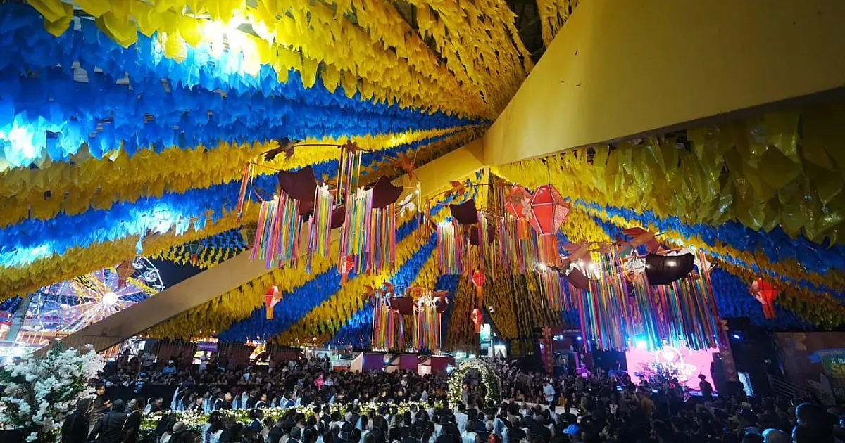 Vista colorida e festiva do Parque do Povo lotado durante a noite, com balões juninos iluminados suspensos no céu e bandeirolas cruzando o espaço