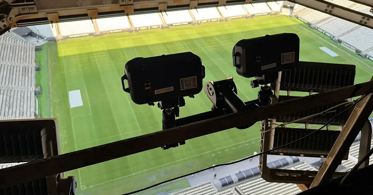Detalhe em plano fechado de uma câmera de monitoramento esportivo moderna instalada sob a cobertura metálica de um estádio de futebol moderno