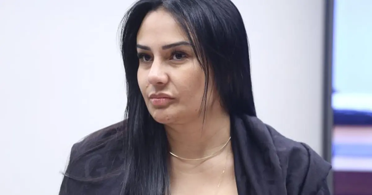 Deputada discursando no plenário da Câmara com microfone à frente e bandeiras ao fundo