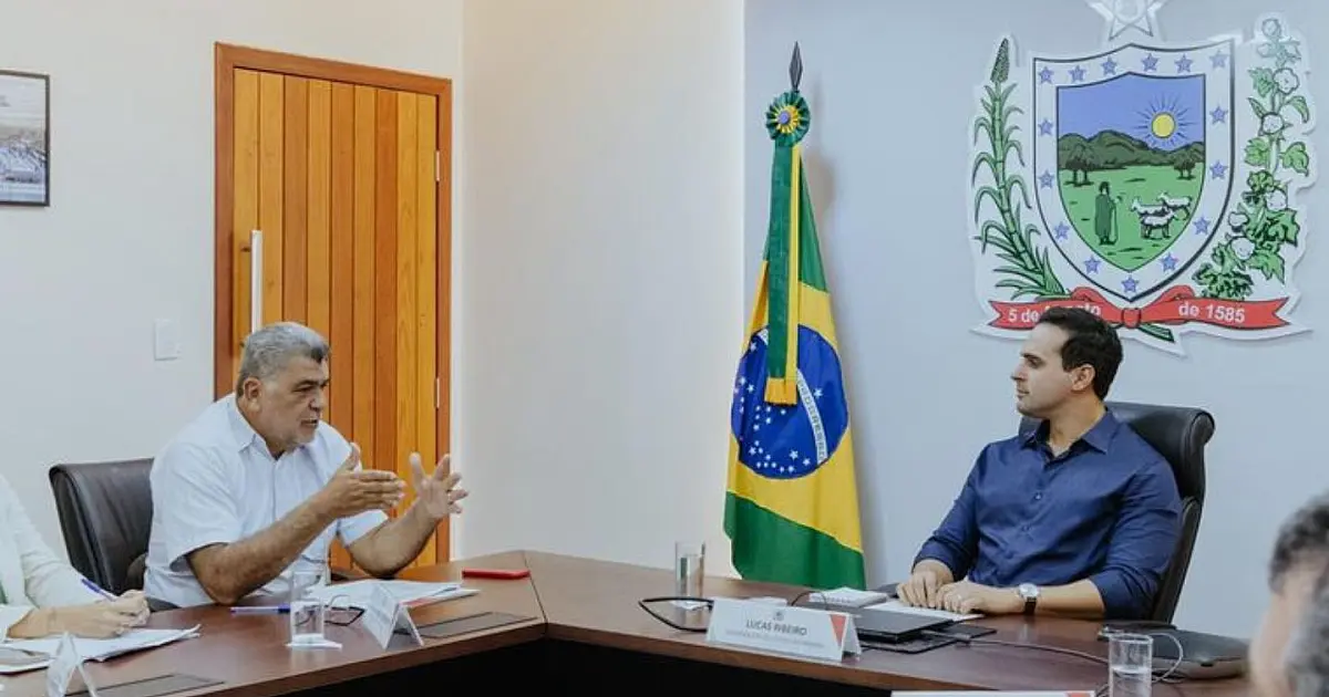 O governador Lucas Ribeiro e o presidente da Funasa, Lenildo Morais, em pé em uma sala de reuniões oficial, sorrindo e posando para a foto enquanto seguram pastas de documentos
