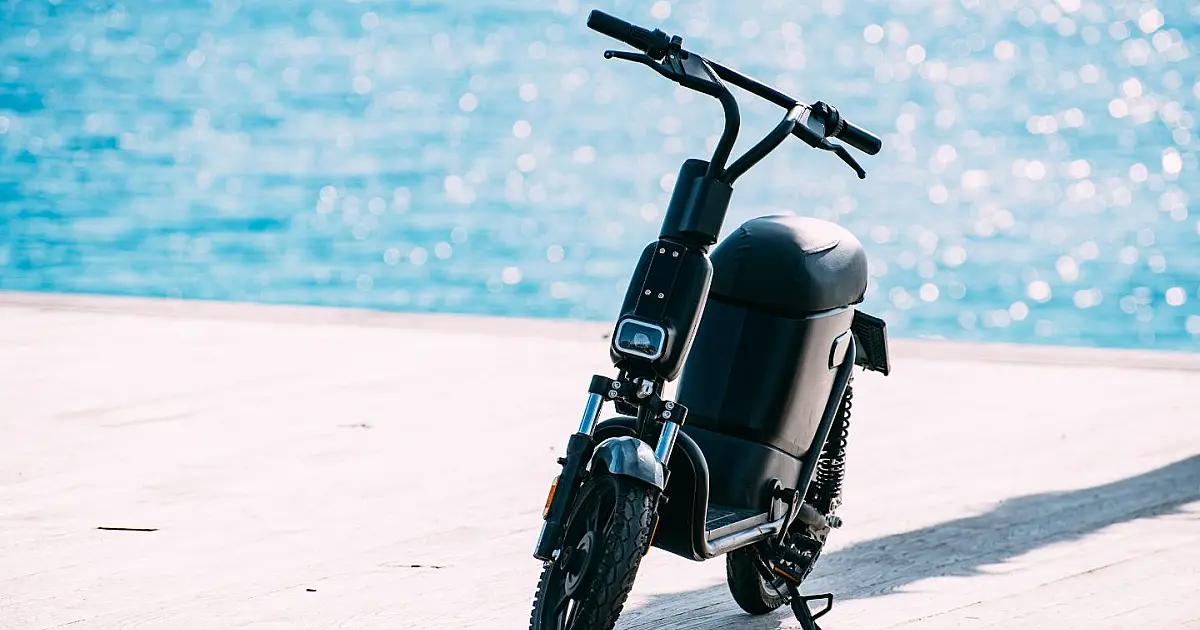 Uma bicicleta elétrica moderna de cor preta estacionada em um suporte urbano de metal em um calçadão, com prédios ao fundo em um dia ensolarado