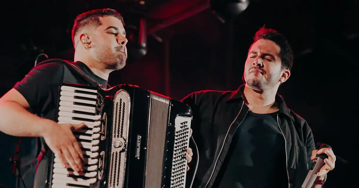 O cantor Jonas Esticado se apresentando com microfone na mão sob luzes coloridas de um grande palco