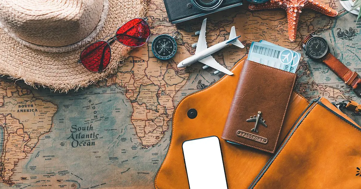 Visão aérea de acessórios de viagem como óculos escuros, passaporte, chapéu de palha e câmera fotográfica organizados sobre um mapa mundial de papel