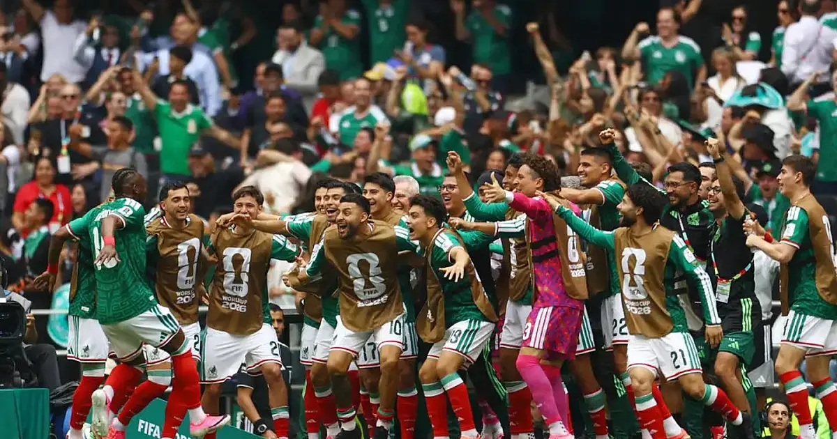 Atletas de camisa verde celebrando um gol abraçados no gramado de um estádio lotado de torcedores.