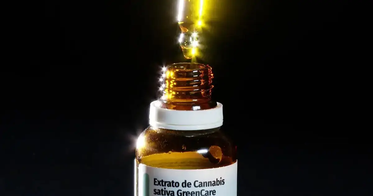 Frascos de vidro âmbar com conta-gotas contendo óleo medicinal dispostos ao lado de um par de halteres em uma sala de ginástica com fundo claro