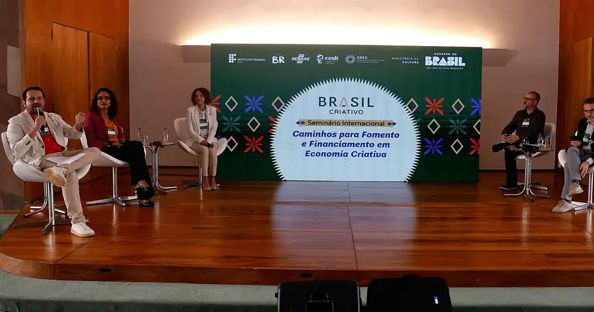 Autoridades e gestores públicos reunidos em uma mesa redonda de debates em um auditório imponente, conversando diante de uma plateia atenta