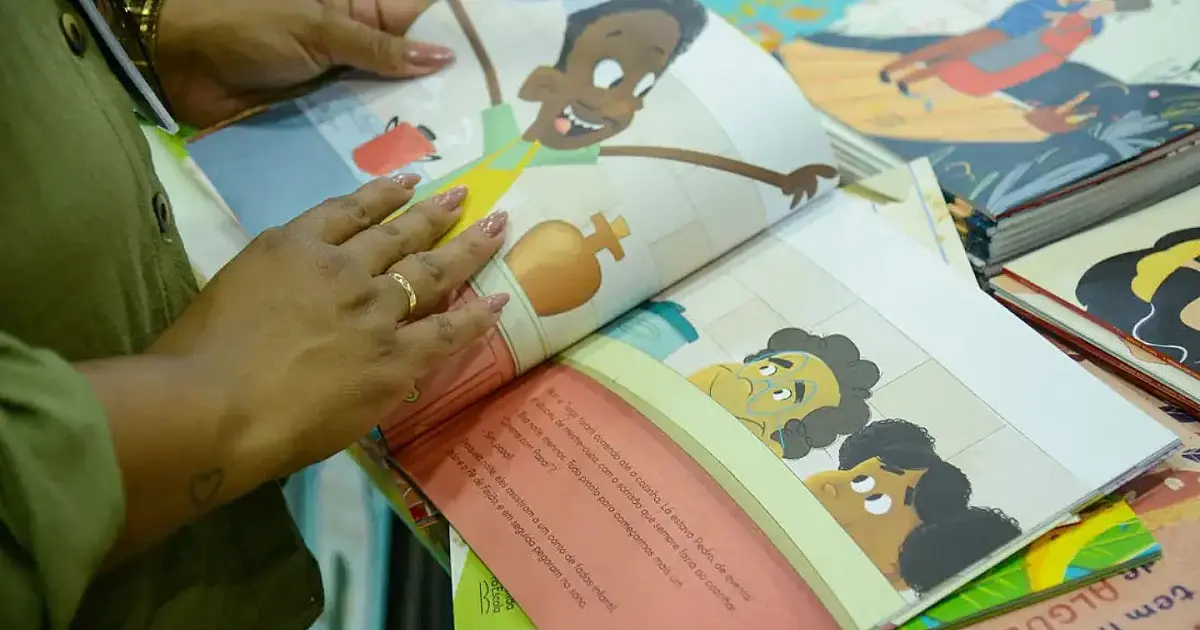 Crianças sentadas no chão de um pátio escolar folheando livros e trocando cromos coloridos de forma animada