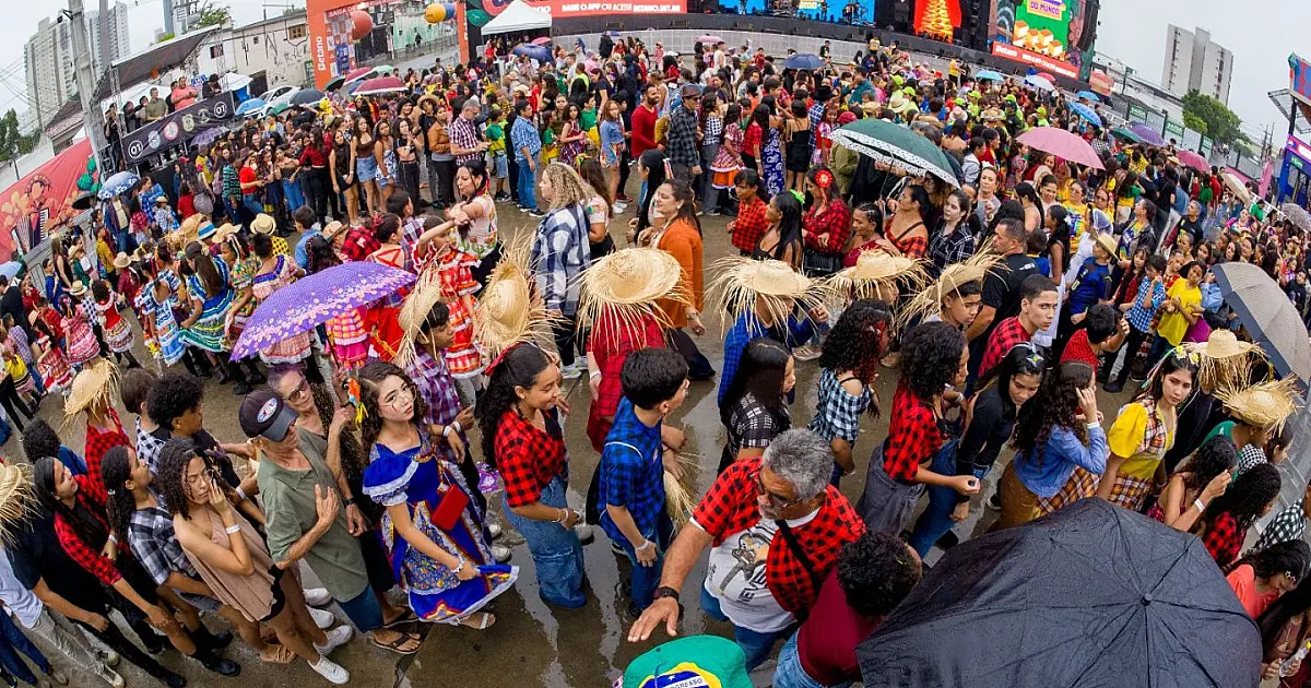 Vista panorâmica do pátio de eventos tomado por centenas de dançarinos com trajes juninos coloridos organizados em círculos