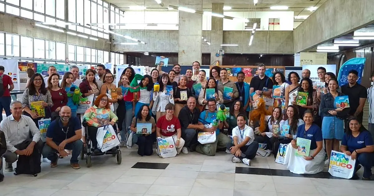 Autoridades e educadores reunidos no palco da Biblioteca Pública exibindo os novos livros de ciência distribuídos pelo governo