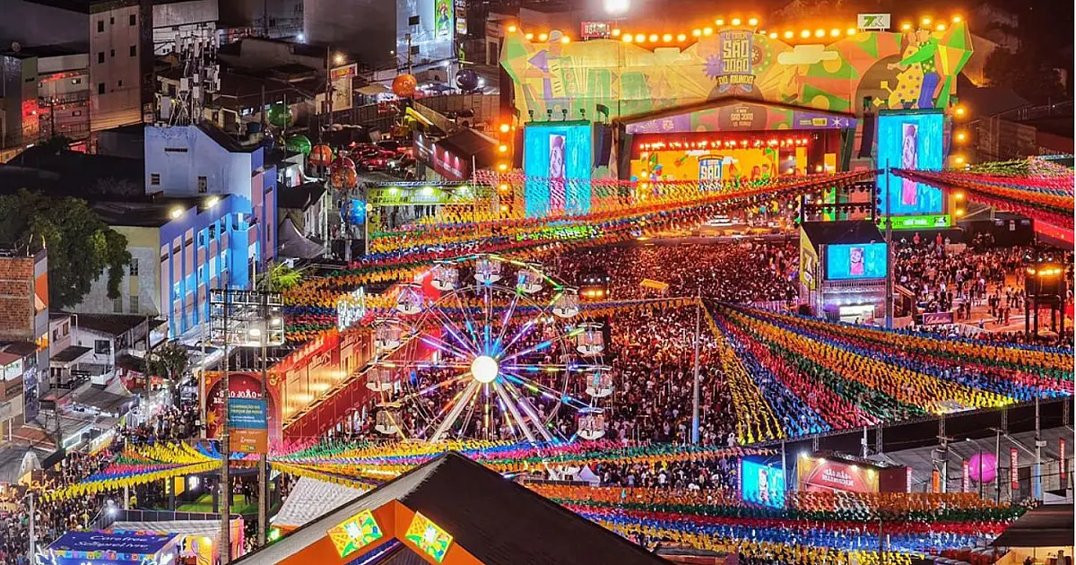 Vista aérea noturna do Parque do Povo completamente iluminado e lotado por uma multidão de pessoas concentradas ao redor do palco principal