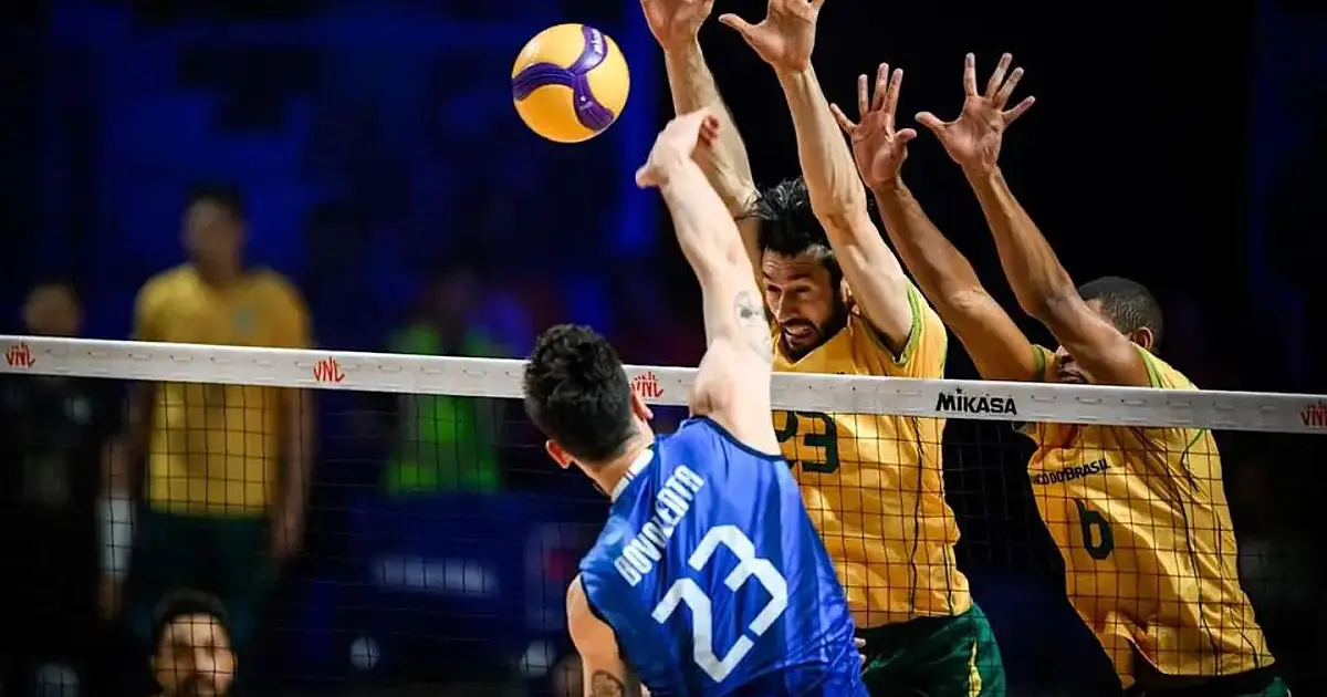 Jogadores da seleção de vôlei saltando na rede para tentar bloquear um ataque adversário em uma quadra oficial de vôlei iluminada