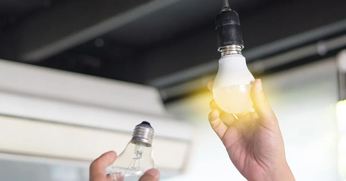 Homem de perfil rosqueando uma nova lâmpada de LED branca no bocal de uma luminária de teto em um ambiente residencial