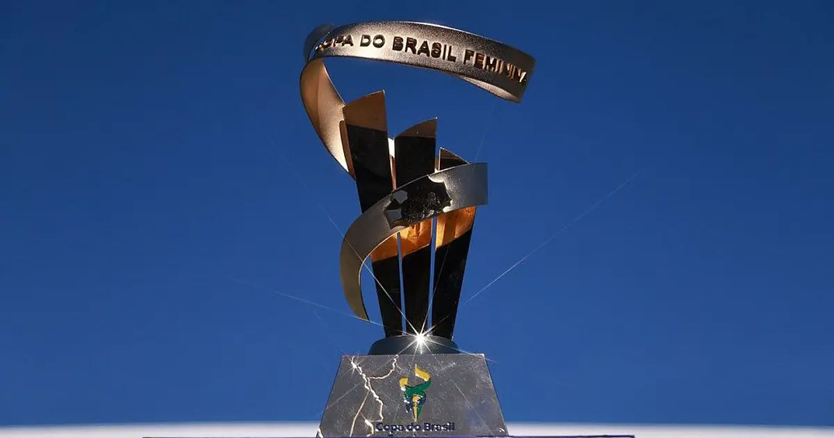 O troféu dourado e prateado da Copa do Brasil de futebol feminino em exposição sobre um pedestal preto em dia de evento