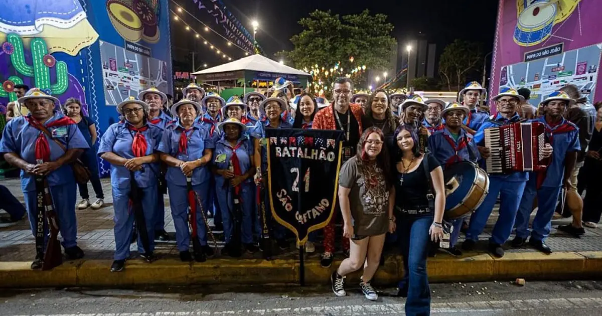 Público concentrado em um polo decorado com bandeirinhas de São João, vestindo camisas do Brasil e assistindo a uma transmissão em um telão