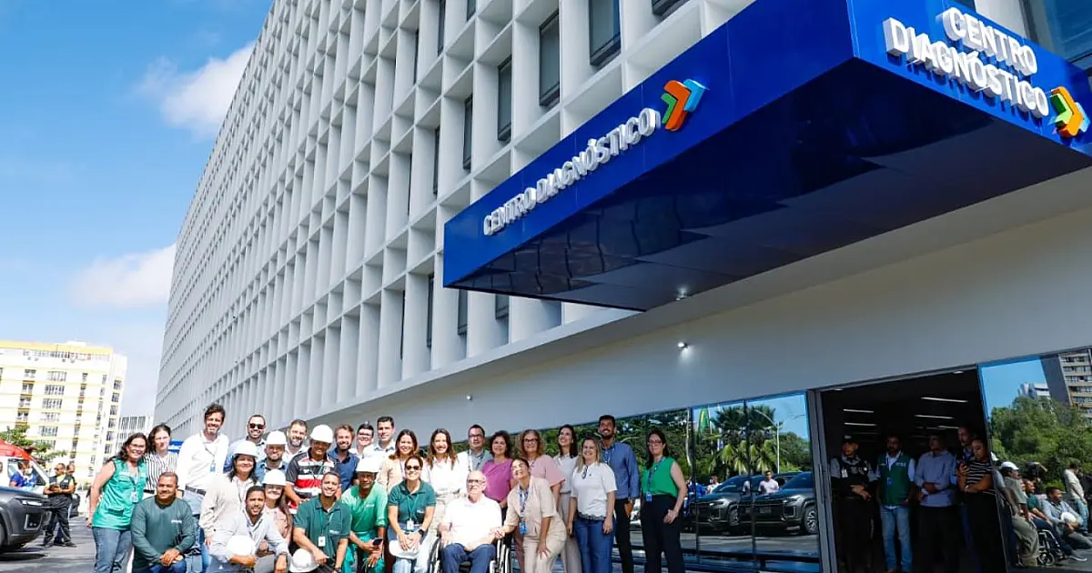 A governadora de Pernambuco vestindo colete oficial e capacete de obra, caminhando ao lado de engenheiros e secretários em um corredor hospitalar em reforma com fiação exposta e paredes rebocadas
