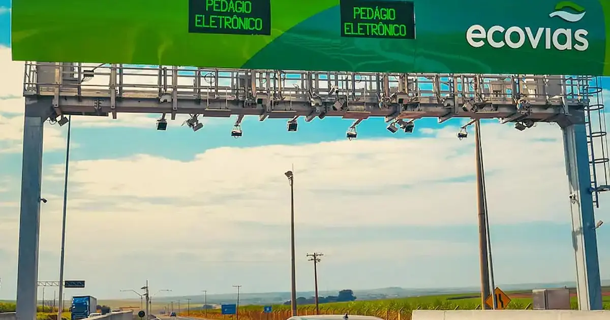 Um pórtico de aço instalado sobre as faixas de rolamento de uma rodovia movimentada sustentando câmeras e antenas eletrônicas