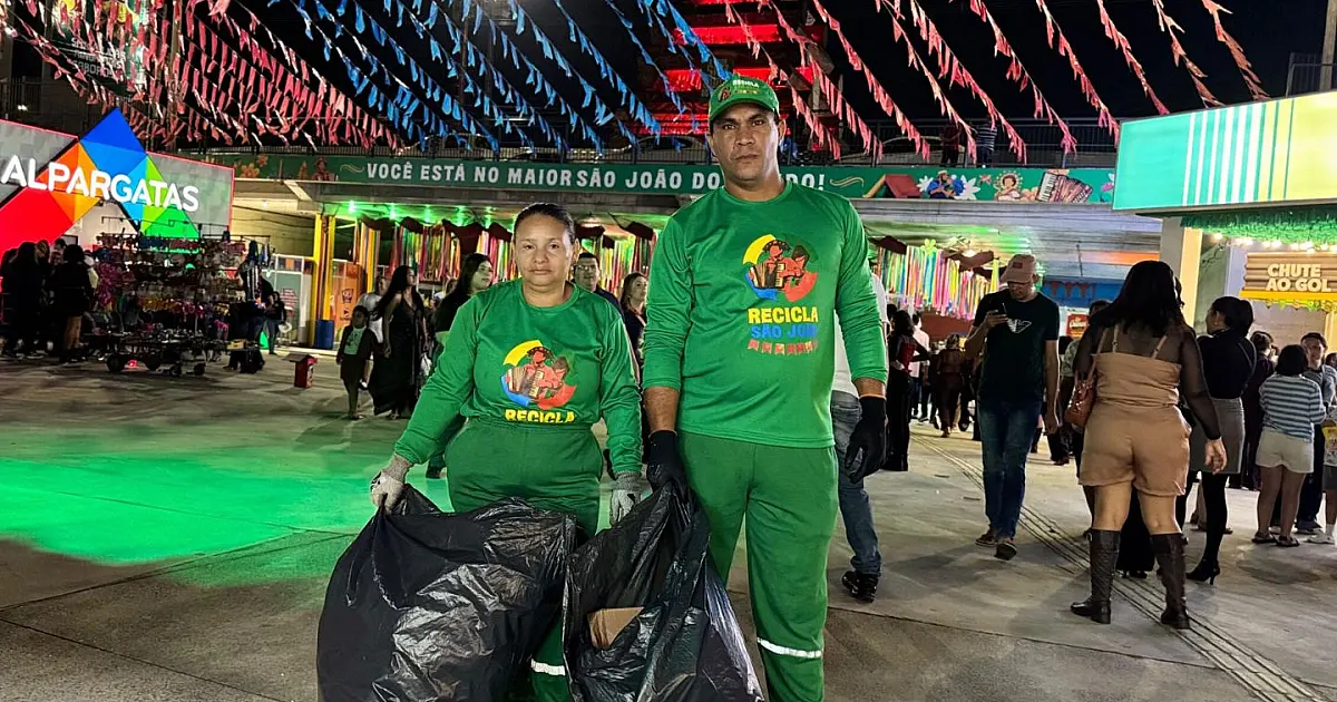 Agente de limpeza urbana vestindo fardamento laranja reflexivo, esvaziando um grande contêiner verde de recicláveis em uma área de triagem durante o dia