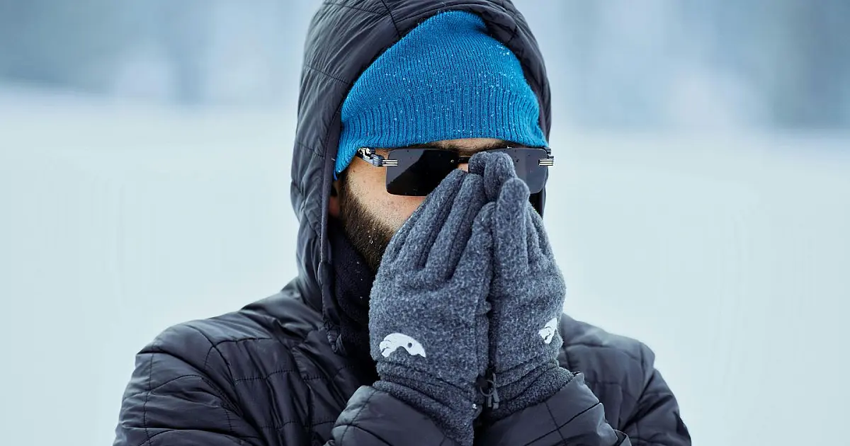 Fotografia em plano médio de um homem agasalhado com casaco pesado de inverno, cachecol e gorro, respirando em um ambiente externo de clima frio com neblina ao fundo.