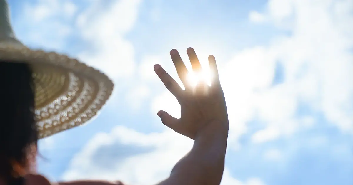 Mulher adulta expressando cansaço e limpando o suor da testa com um lenço sob um dia ensolarado e de calor intenso na cidade