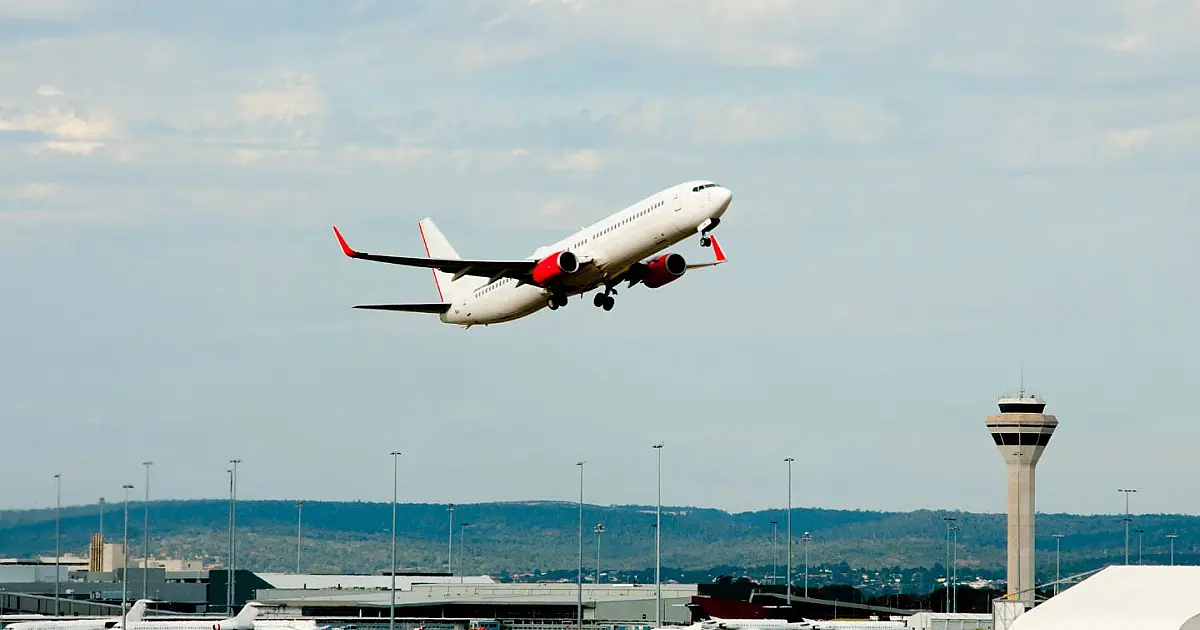 Aeronave comercial de grande porte decolando em direção ao céu azul com a pista do aeroporto ao fundo
