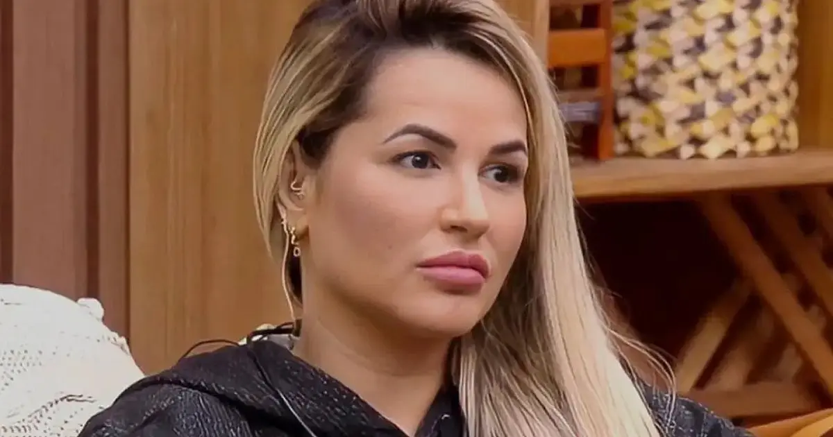 Mulher loira de óculos escuros e blazer preto posando em um ambiente interno iluminado