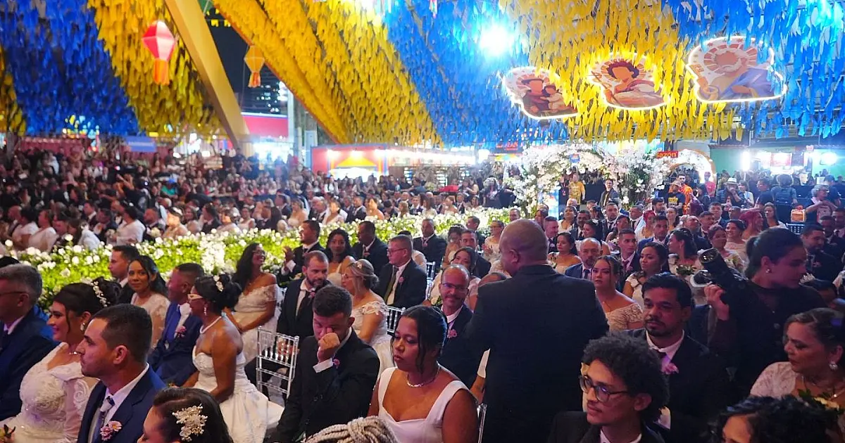 Vista ampla do interior da Pirâmide do Parque do Povo com dezenas de casais vestidos de noivos e noivas sentados e organizados para a cerimônia.