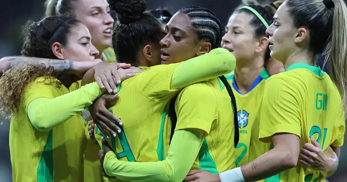 Jogadoras da Seleção Brasileira Feminina abraçadas em um círculo no centro do gramado, vestindo a tradicional camisa amarela e calções azuis, durante comemoração de gol