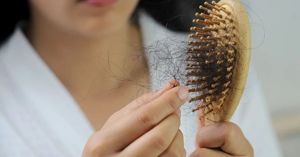 Mulher jovem vista de perfil deitada em uma cama confortável com semblante preocupado enquanto observa as pontas ressecadas do próprio cabelo