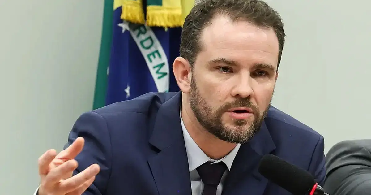 O ministro Dario Durigan falando de forma compenetrada durante uma transmissão de rádio em um estúdio jornalístico