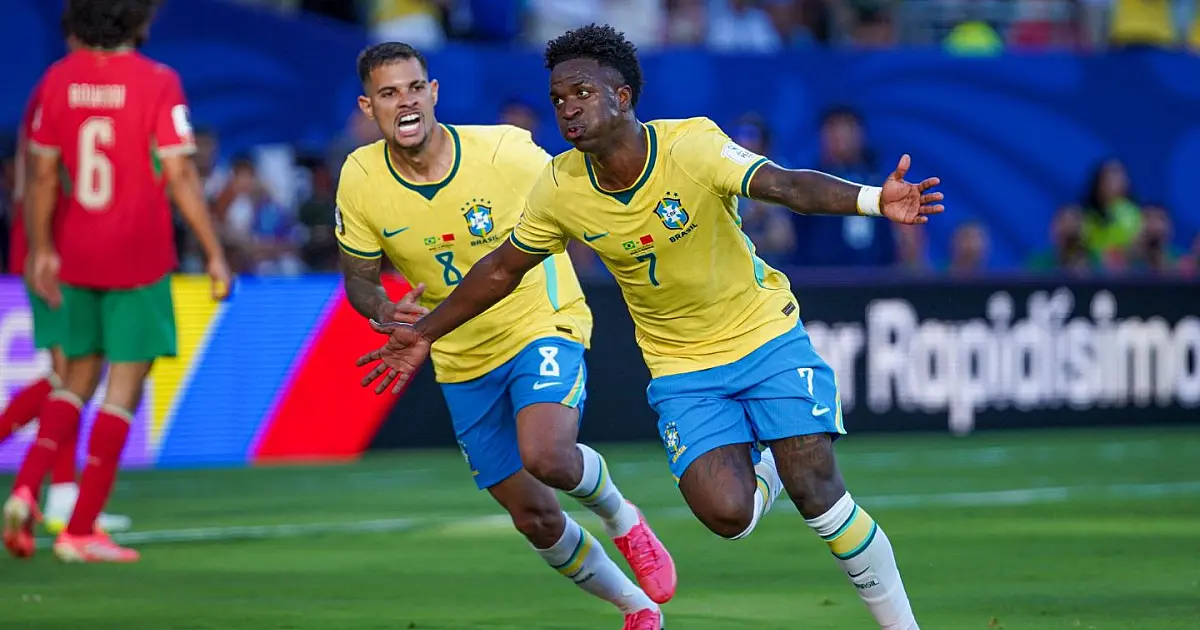 O atacante Vinícius Júnior correndo pelo gramado com os braços abertos, vestindo o uniforme oficial azul e branco da Seleção Brasileira