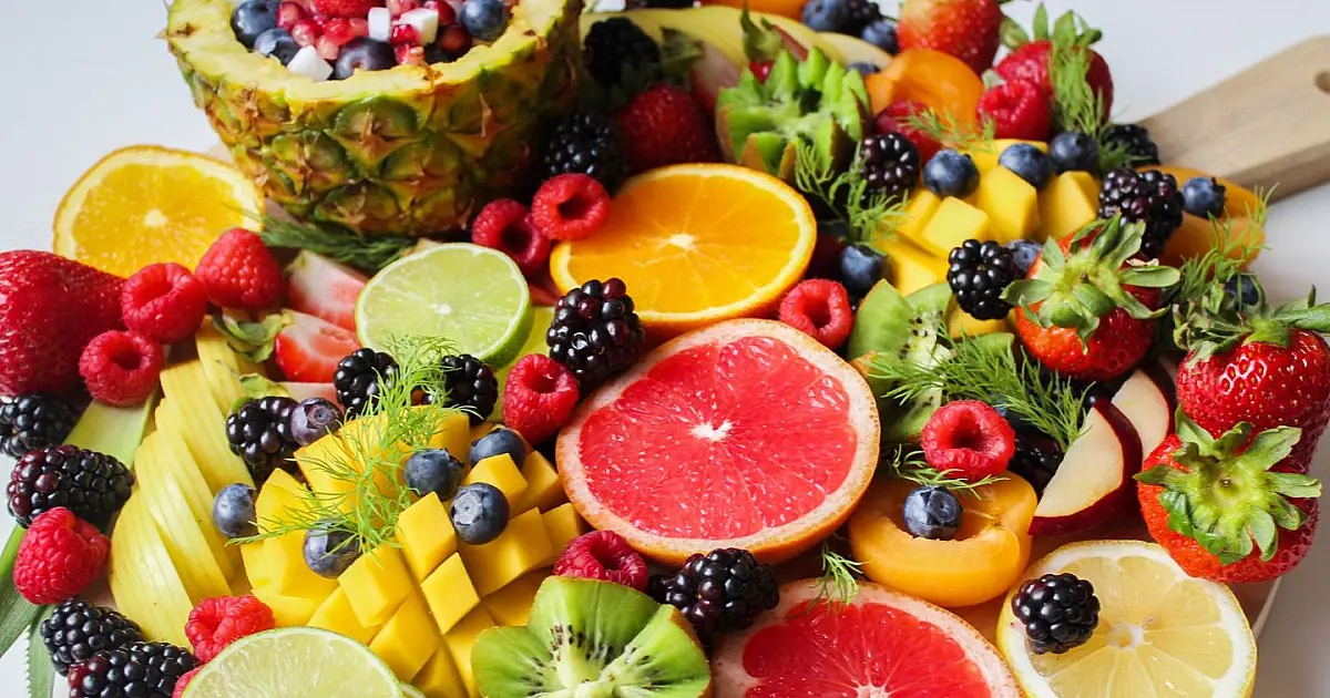 Pedaços cortados de frutas coloridas como morango, kiwi, manga e abacaxi organizados sobre uma bandeja de madeira
